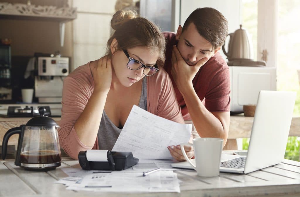 A couple study their finances with a fresh cup of coffee next to it.