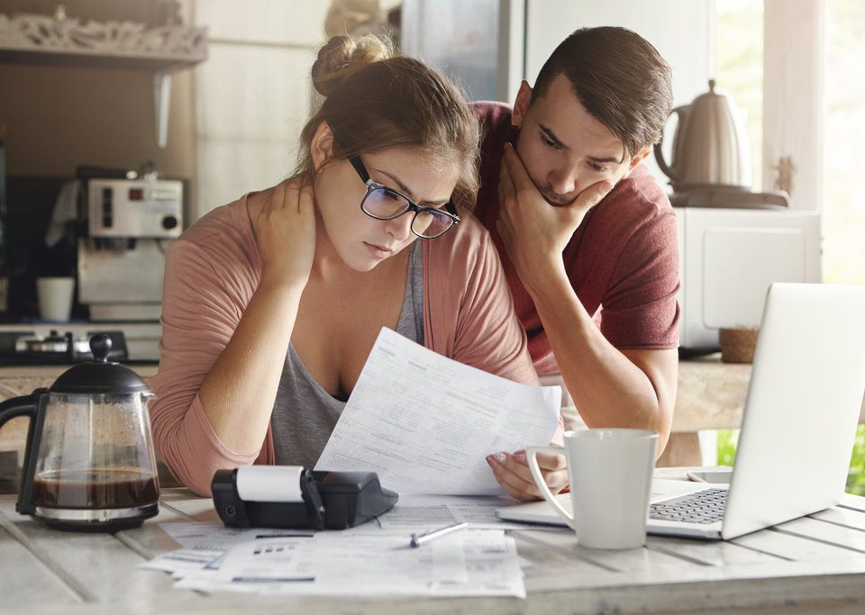 A couple study their finances with a fresh cup of coffee next to it.