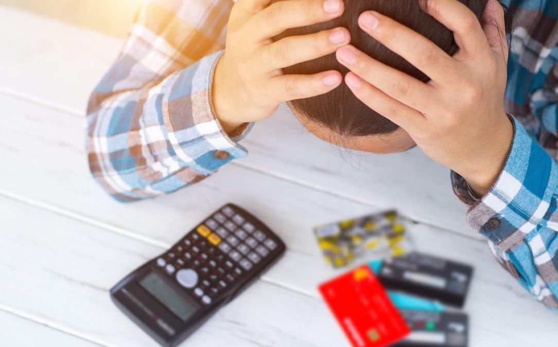 An image of a man holding his head and looking at a stack of credit cards.