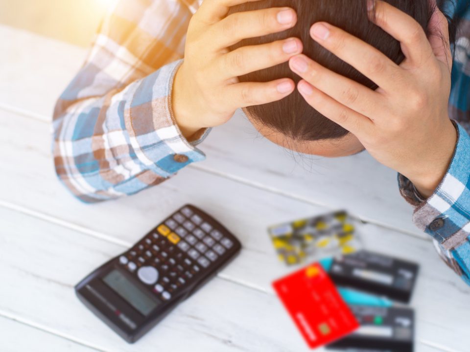 An image of a man holding his head and looking at a stack of credit cards.