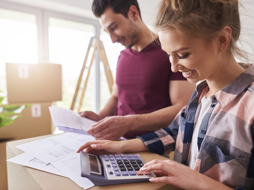 An image of two people moving into a house, doing quick sums on a calculator.