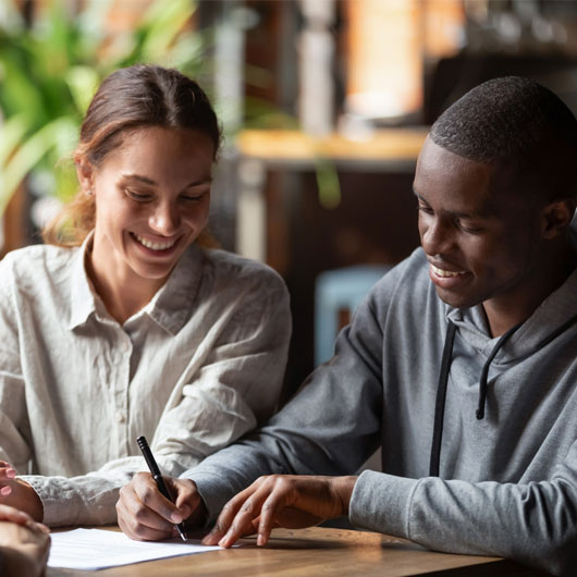 An image of a young couple signing documents, smiling.