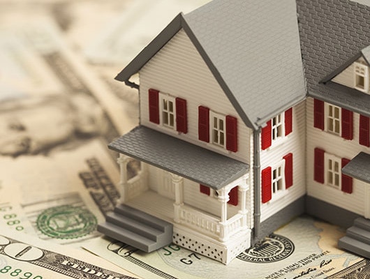 An image of a small toy house laid out on top of American money.