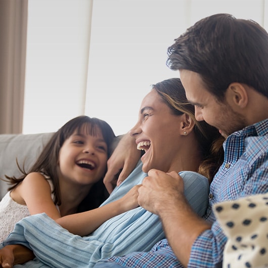 A family laughs and cuddles on the couch.