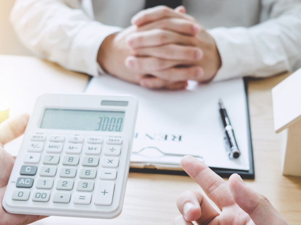 An image of a person gesturing to a calculator while talking with someone.