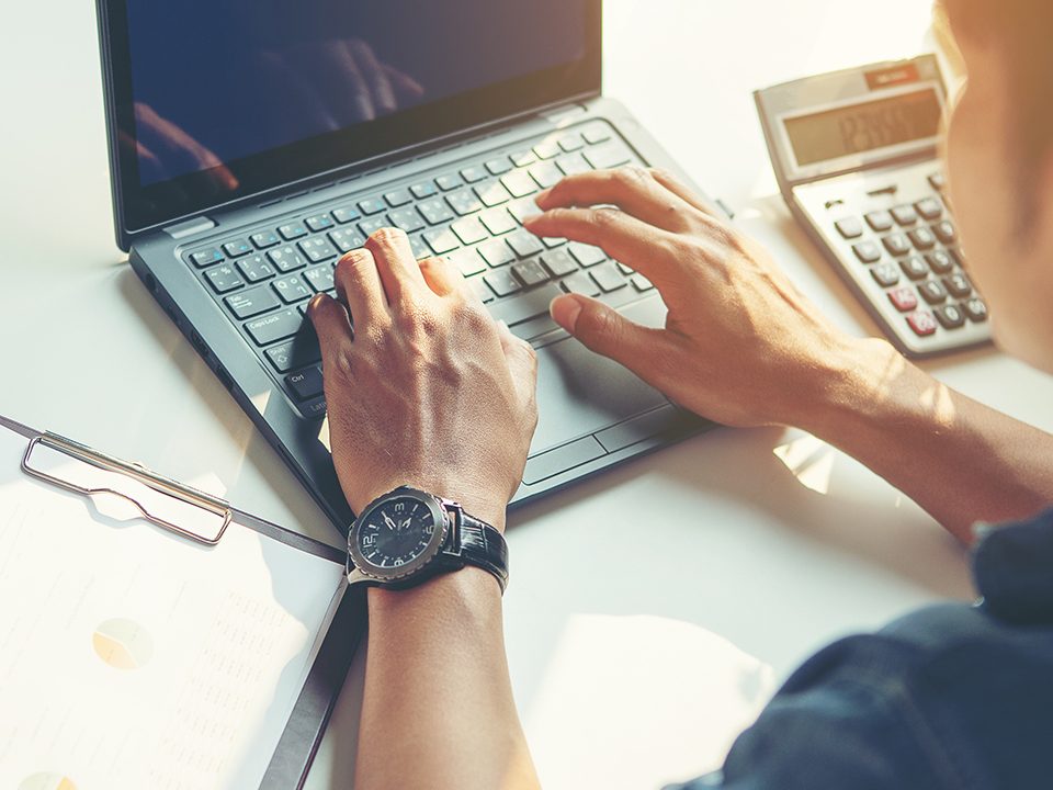 A young man works on a laptop in the sunshine.