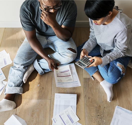 A couple sit on the ground doing calculations surrounded by documents.