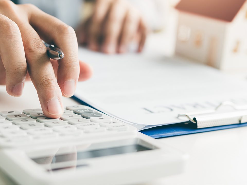 A hand holding a pen types on a calculator