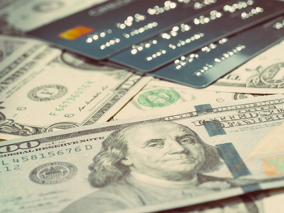 An image of several hundreds laid out under a stack of credit cards.