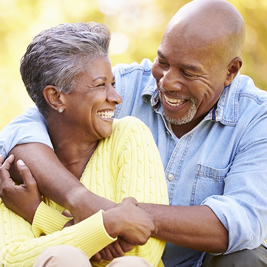 An older black couple hold each other, smiling.