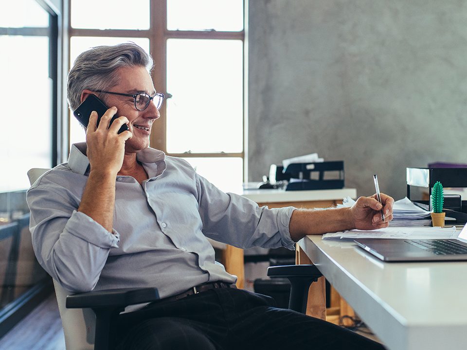 An older man smiles while on the phone.