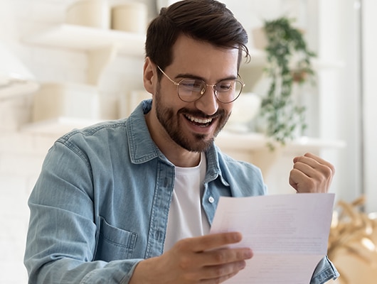 A young man with glasses smiling at a document.